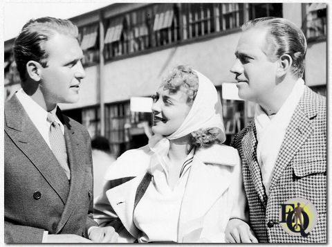 Weerzien bij Columbia! Melvyn Douglas (rechts), die Virginia Bruce, zijn tegenspeelster in de Columbia-film "Women of Glamour", naar de set begeleidt, komt zijn oude vriend Ralph Bellamy tegen. Tien jaar geleden waren Douglas en Bellamy nog rivaliserende impresario's van vaste toneelgezelschappen; tegenwoordig staan ​​ze beiden onder langdurig contract bij Columbia (rond feb 1937).