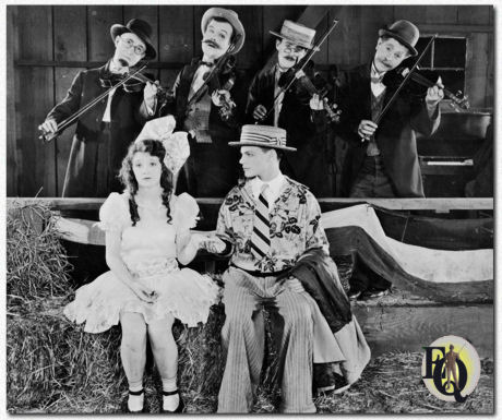 The first Day-Quillan collaboration was A Love Sundae (1926), where country girl Day finds her sweetheart O’Shea has fallen for an alluring city girl. She attempts to get him back by eloping with Quillan, a bashful soda jerk. Lost today, tantalizing stills show that the centerpiece of the short was a Halloween-themed barn dance with streamers and strings of papier-maché jack-o’-lanterns hanging from the ceiling. Day appears in a frilly “little girl” outfit while surrounded by fashionable fellow teens, suggesting there’s a gag where she’s the only one who shows up to the dance in a costume.