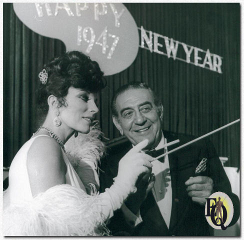Joan Collins (Lady Daisy Frawley) waves a cigarette holder, attempting to learn Guy Lombardo's baton technique.